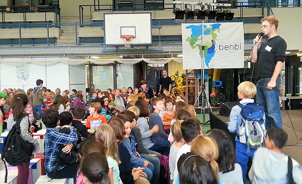Moderator auf der Bühne spricht auf einer benbi-Veranstaltung zu Schülerinnen und Schülern.